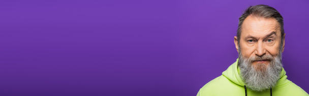 skeptical senior man moving eyebrow while looking at camera on purple background, banner - Photo, Image