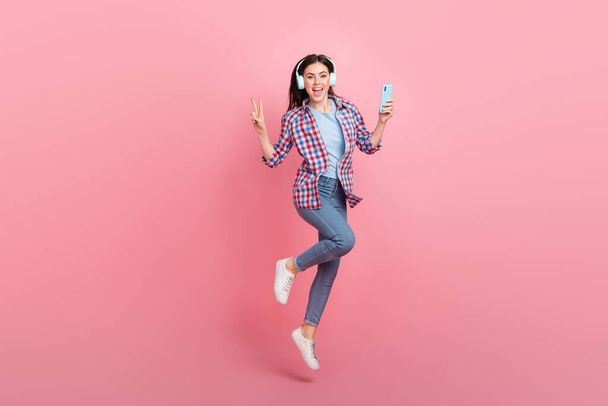 Full size photo of good mood overjoyed lady show v-sign say hello surfing in phone isolated on pink color background. - Fotó, kép
