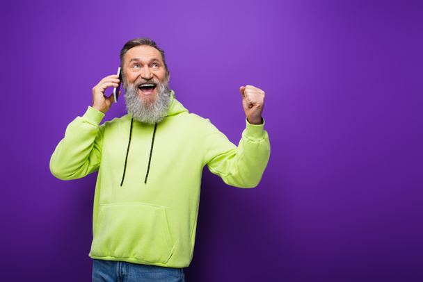 animado homem sênior com barba e cabelos grisalhos falando no smartphone em roxo  - Foto, Imagem