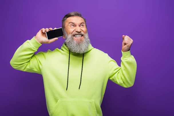 amazed senior man holding smartphone with blank screen isolated on purple  - Zdjęcie, obraz