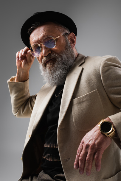 portrait of bearded senior man in stylish beige jacket and derby hat on grey - Fotoğraf, Görsel