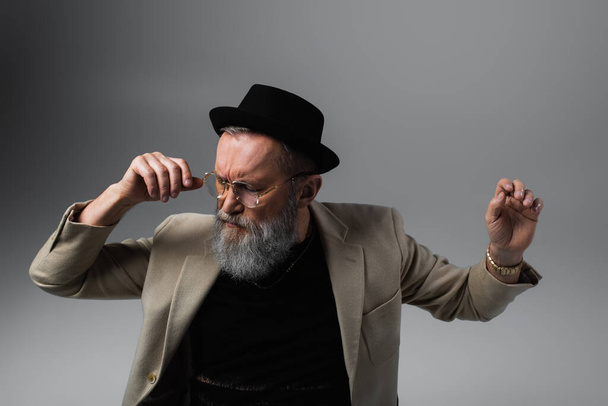 bearded senior man in derby hat and eyeglasses gesturing on grey - Fotografie, Obrázek