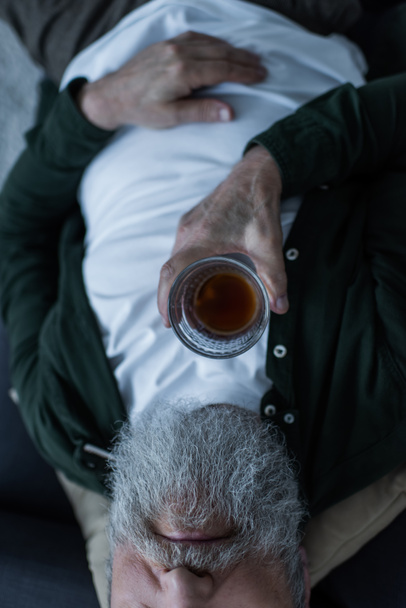 rajattu näkymä onneton vanhempi mies parta makaa sohvalla lasi viskiä kärsiessään kriisi  - Valokuva, kuva