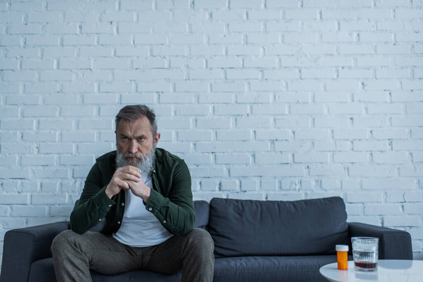 masentunut vanhempi mies harmaat hiukset istuu sohvalla lähellä pullon lääkitys ja lasi viskiä sohvapöytä - Valokuva, kuva