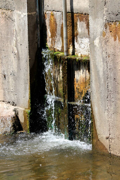 Wycieki zamknięte stare częściowo zardzewiałe metalowe bramy rzeki pokryte mech i brud zbudowany między grubymi betonowymi i kamiennymi ścianami tamy trzymając spokojną rzekę w ciepły słoneczny wiosenny dzień - Zdjęcie, obraz