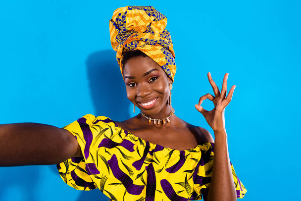 Photo de jeune femme africaine gaie étonnante prendre selfie montrant signe OK isolé sur fond de couleur bleue. - Photo, image