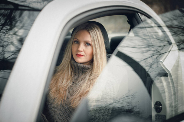 Opera d'arte. Una foto di una bella ragazza elegante seduta in macchina. Ci sono bellissimi riflessi sui finestrini della macchina. - Foto, immagini