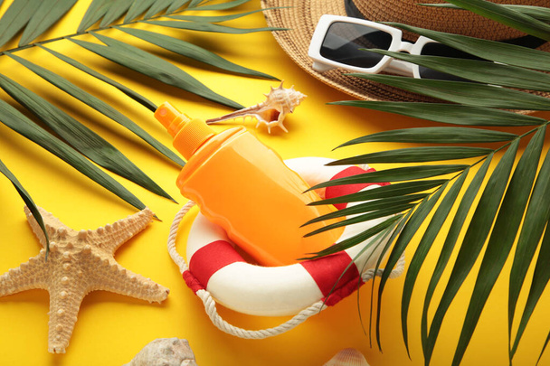 Lifebuoy with sunscreen and palm leaf on yellow background. Summer concept. Top view - Photo, image