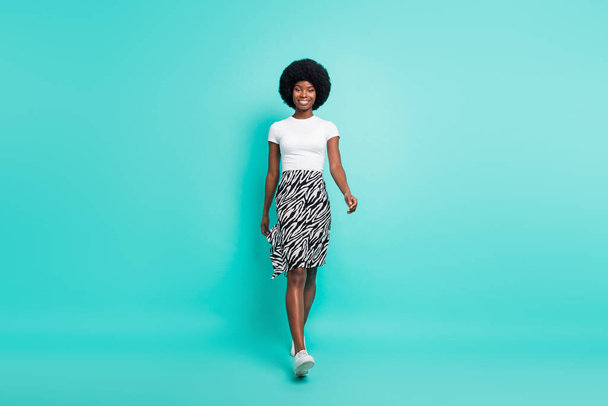 Photo of excited charming dark skin woman dressed casual outfit walking smiling isolated turquoise color background. - Foto, Imagem