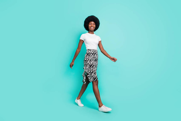 Foto de cuerpo completo de la bella dama afro americana feliz caminar vacío espacio sonrisa aislada sobre fondo de color verde azulado. - Foto, imagen
