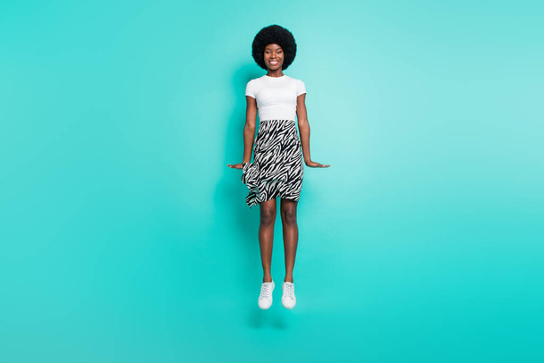 Photo of charming sweet dark skin woman dressed casual outfit jumping high smiling isolated turquoise color background. - Photo, Image