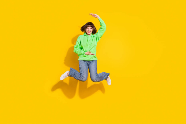 Full size photo of happy pretty lovely lady jump up hold hand measure empty space isolated on yellow color background. - Foto, Imagem