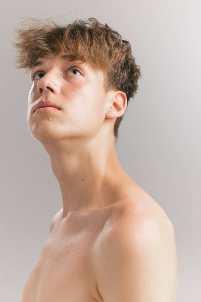 Looking up. Beauty portrait of young man, teen isolated on grey studio background. Concept of teenage skin care, health, cosmetics for problem skin, youth. Art, fashion, healthy lifestyle and ad - Valokuva, kuva