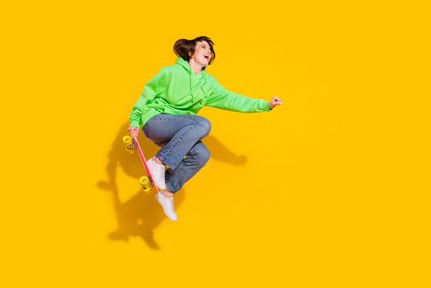 Full length body size view of attractive cheerful girl jumping riding skate isolated over bright yellow color background. - Foto, afbeelding