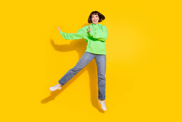 Фотографія повного тіла привабливої молодої щасливої жінки, що стрибає вгору посмішкою повсякденного вбрання ізольовано на жовтому кольорі
. - Фото, зображення