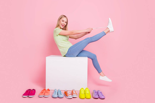 Photo of cheerful blonde lady sit podium tie shoelaces have fun wear green t-shirt jeans isolated on pink background. - Photo, Image