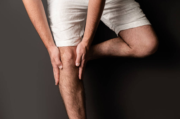 白い背景に痛みの中で手で膝をつかんで強い運動脚を持つ若いスポーツマン - 写真・画像