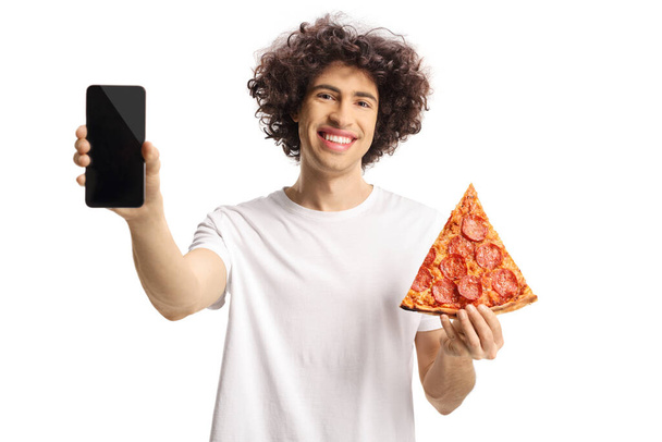 Wesoły młody człowiek trzyma kawałek pizzy i pokazuje smartfona odizolowanego na białym tle - Zdjęcie, obraz