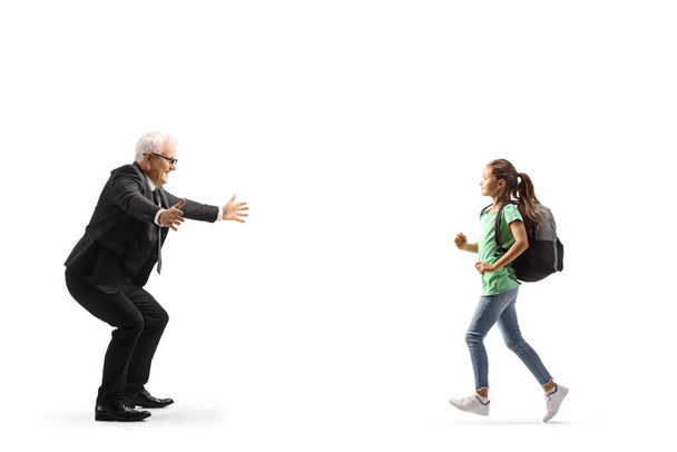 Full length profile shot of a schoolgirl running towards her father for a hug isolated on white background - Фото, зображення
