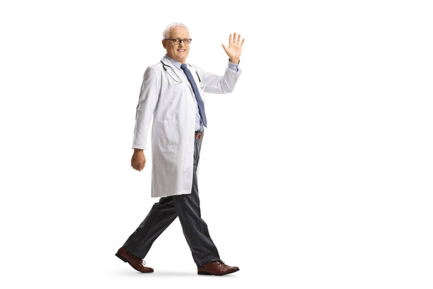 Full length shot of a mature male doctor walking and waving isolated on white background - Fotó, kép