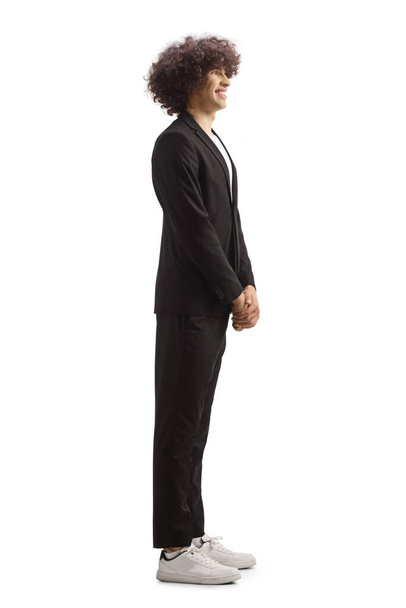 Full length profile shot of a smiling young man in a black suit standing and waiting isolated on white background - Foto, afbeelding