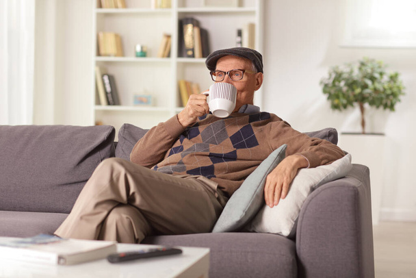 Elderly man relaxing on a sofa at home and drinking a cup of tea - Fotografie, Obrázek