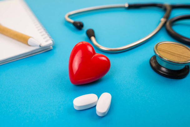 Health concept. Red heart with a stethoscope and pills on a blue background. - Foto, afbeelding