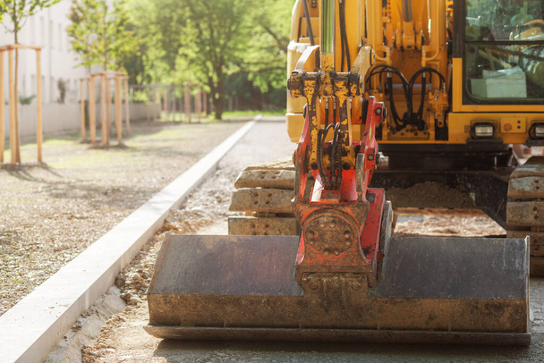 Excavator Constructs New Sidewalk in park. Excavator works with wide bucket. Road works.  - 写真・画像