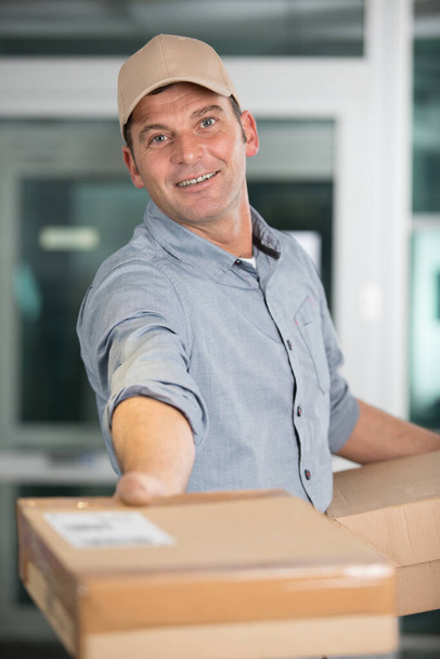 happy delivery man giving parcel to the camera - Zdjęcie, obraz