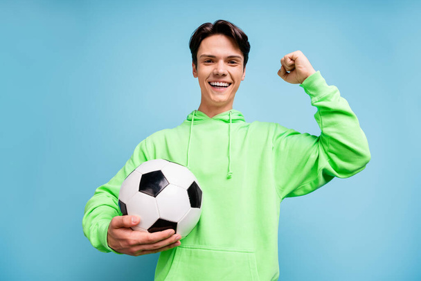 Photo of attractive lucky young gentleman wear green sweatshirt smiling holding ball rising fist isolated blue color background. - 写真・画像