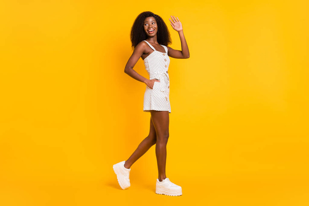 Full size photo of dark skin young lady go empty space wave hello isolated on yellow color background. - Valokuva, kuva