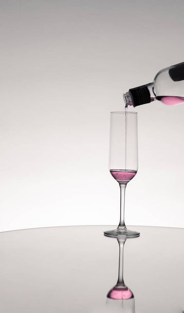 The red wine poured into a glass from the bottle mirrored on the table - 写真・画像