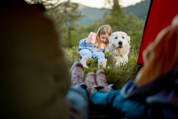 Nettes kleines Mädchen umarmt mit einem Hund, während es mit seinen Eltern in der Natur unterwegs ist, Blick von innen auf das Zelt. Kindheit, Freundschaft mit Haustieren - Foto, Bild