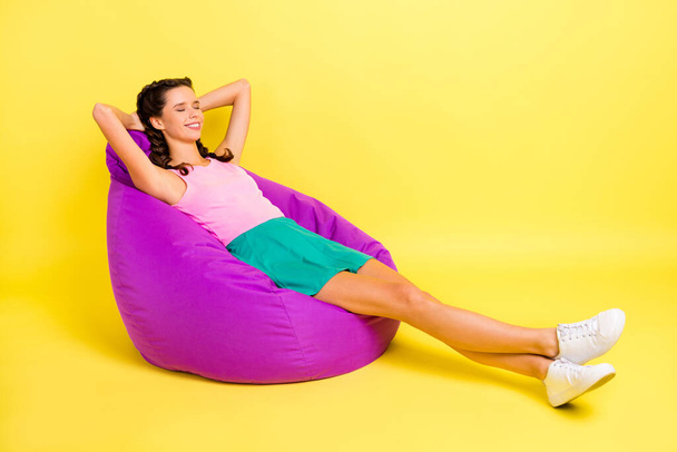 Full body profile side photo of relaxed young woman hold hands behind head lie bean bag isolated on vibrant yellow color background. - Zdjęcie, obraz