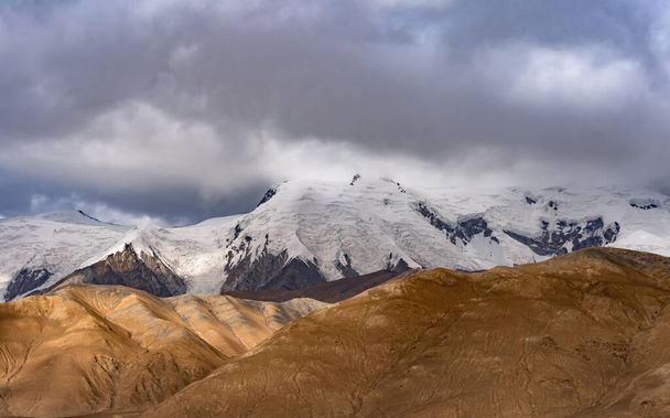 A beautiful landscape view of sandy hills and snowy mountains under a cloudy gray sky - Foto, immagini