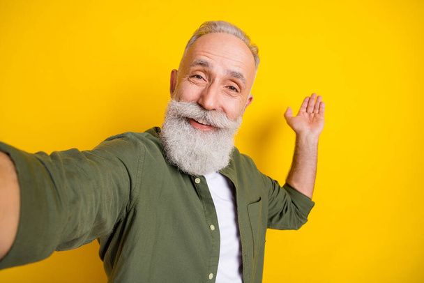 Photo portrait of grandfather taking selfie smiling showing blank space on palm isolated vibrant yellow color background. - Fotó, kép