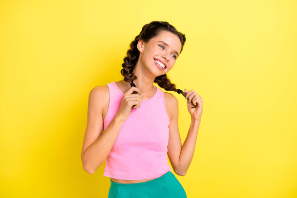 Photo of cheerful charming young woman hold hands braids look empty space happy summer isolated on yellow color background. - Foto, afbeelding