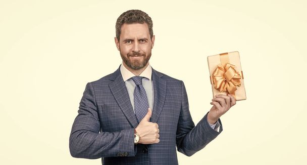 усміхнений бізнесмен у костюмі тримає подарункову коробку показати великий палець вгору ізольовано на білому, найкращий подарунок
. - Фото, зображення