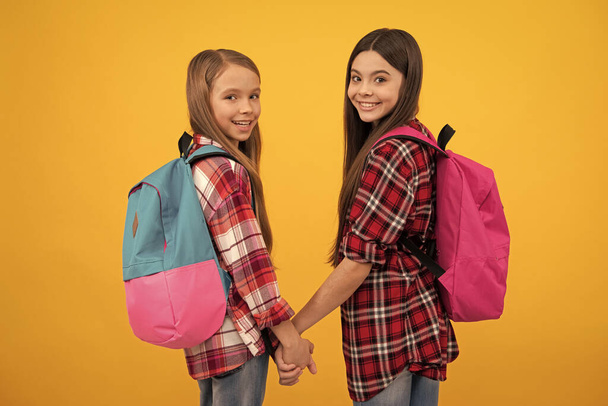 Mutlu çocukluk. Okul çantalı çocuklar. Güzel genç kızlar sırt çantası taşır. Okula dönüyorum. Bilgi günü. Eğitim konsepti. Sarı arka planda uzun saçlı çocuklar. Eylül 1. - Fotoğraf, Görsel