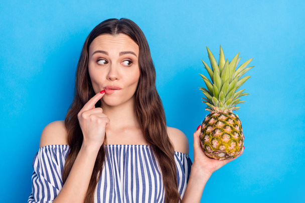 Photo of charming guilty young woman dressed striped outfit finger biting lip looking fruit isolated blue color background. - Foto, afbeelding