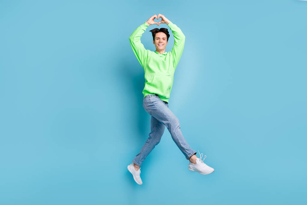 Photo of romantic boyfriend jump fingers show heart symbol wear green hoodie jeans shoes isolated blue color background. - Fotó, kép
