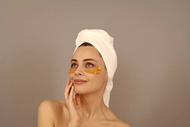 Keep your Skin on dieting. young woman in terry towel use patch. beauty day in spa. applying golden anti-fatigue mask. girl reduce eye bags. skincare. facial collagen cosmetic. moisturizing skin. - Photo, Image