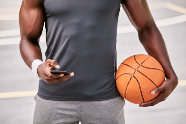 Κλείσιμο ενός παίκτη μπάσκετ γραπτών μηνυμάτων σε ένα τηλέφωνο, ενώ κάνουν ένα διάλειμμα από το να παίζουν έναν αγώνα σε ένα αθλητικό γήπεδο έξω. Χέρια ενός αθλητή που περιηγείται στα μέσα κοινωνικής δικτύωσης σε απευθείας σύνδεση κατά τη διάρκεια ενός διαστήματος παιχνιδιού. - Φωτογραφία, εικόνα