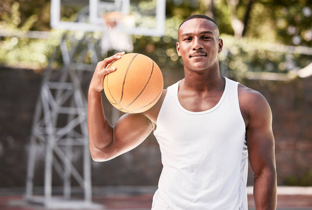 Portrait of a young black male basketball player holding a ball, playing a match on a local sports court outside. One cool muscular man with attitude taking a break to play a fun recreational game. - Foto, Bild