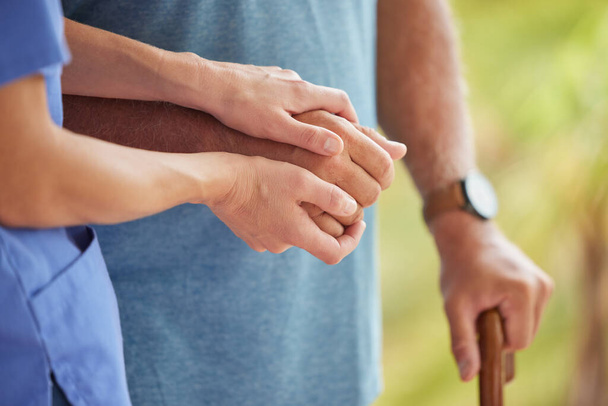 A nurse and senior patient holding hands while helping him to walk outside. Closeup of an elderly man being supported by female caregiver while walking to improve his mobility, health, and wellbeing. - Photo, Image