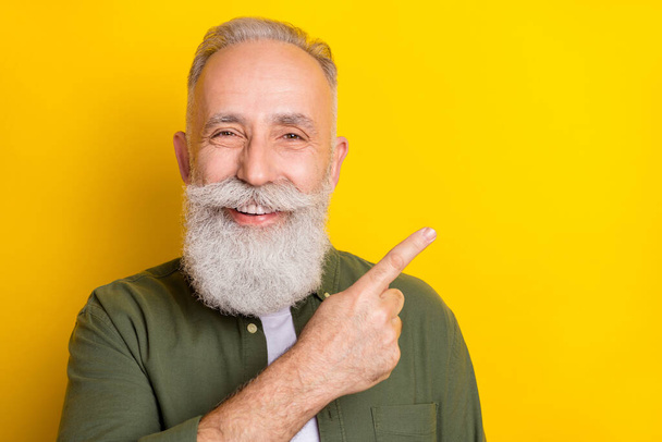 Photo portrait of elder man pointing blank space with finger recommending isolated vivid yellow color background. - Fotografie, Obrázek