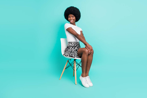 Photo of charming cute dark skin woman dressed casual outfit sitting chair smiling isolated turquoise color background. - Foto, imagen