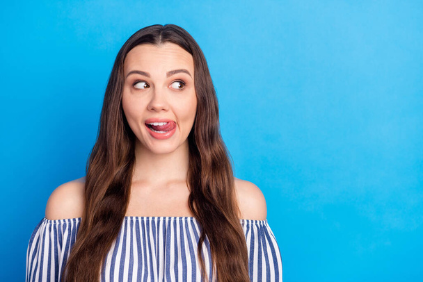 Photo of shiny charming young woman dressed striped outfit smiling licking lips looking empty space isolated blue color background. - Foto, Imagem
