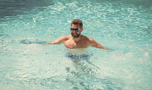 vidám jóképű férfi szemüvegben úszás medencében nyáron, spa. - Fotó, kép