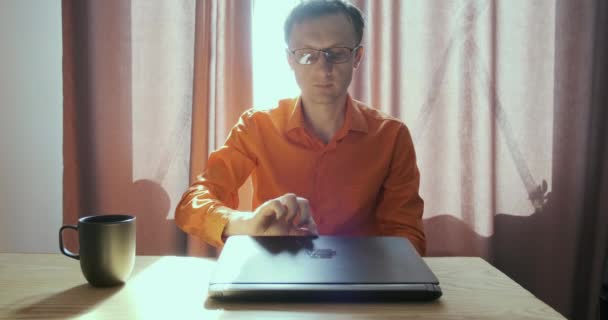 Ο νεαρός αρχίζει να δουλεύει σε λάπτοπ. Ανοίγει το laptop, κάθεται στο γραφείο στο παράθυρο με φως. Έννοια της εργασίας στο σπίτι, ελεύθερος επαγγελματίας, μελέτη, απομακρυσμένη εργασία, καραντίνα. Υψηλής ποιότητας 4k πλάνα - Πλάνα, βίντεο